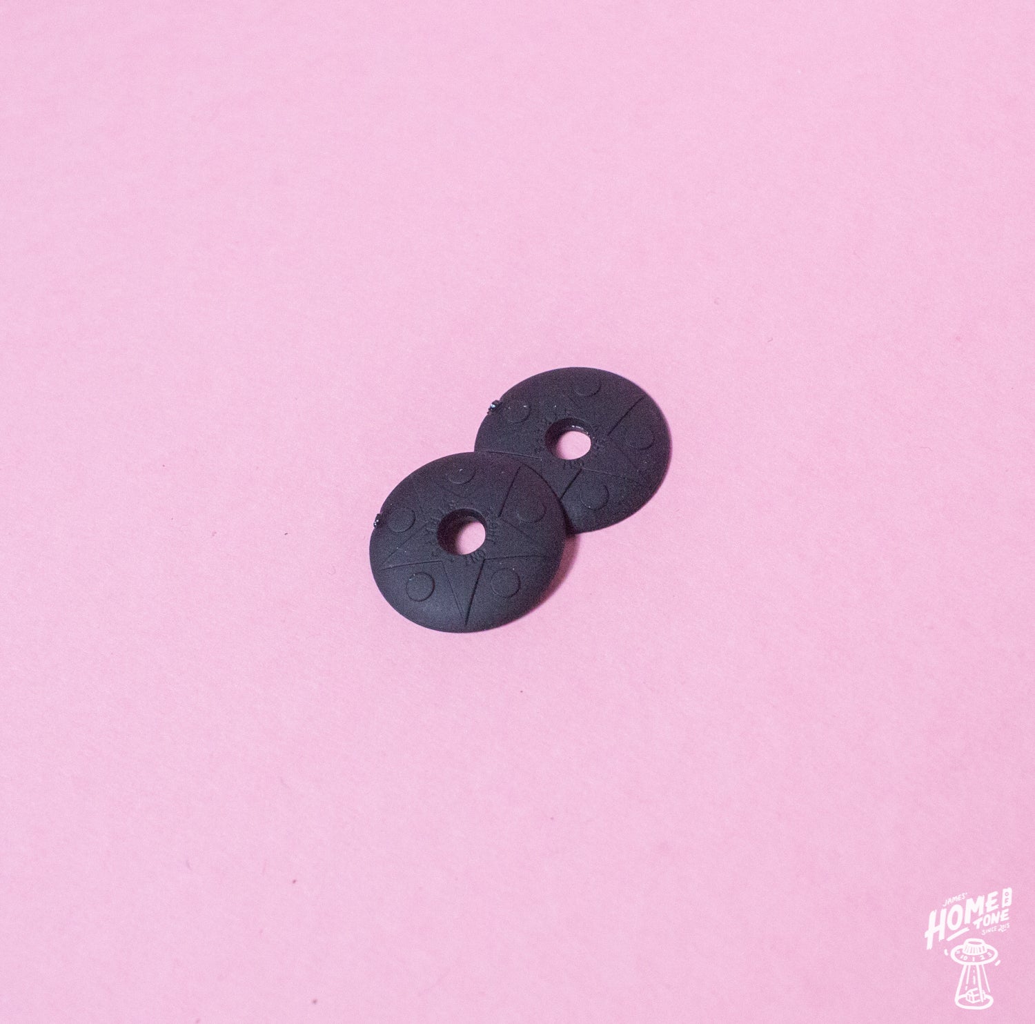 A pair of black rubber strap locks for guitars or basses, displayed on a pink background.