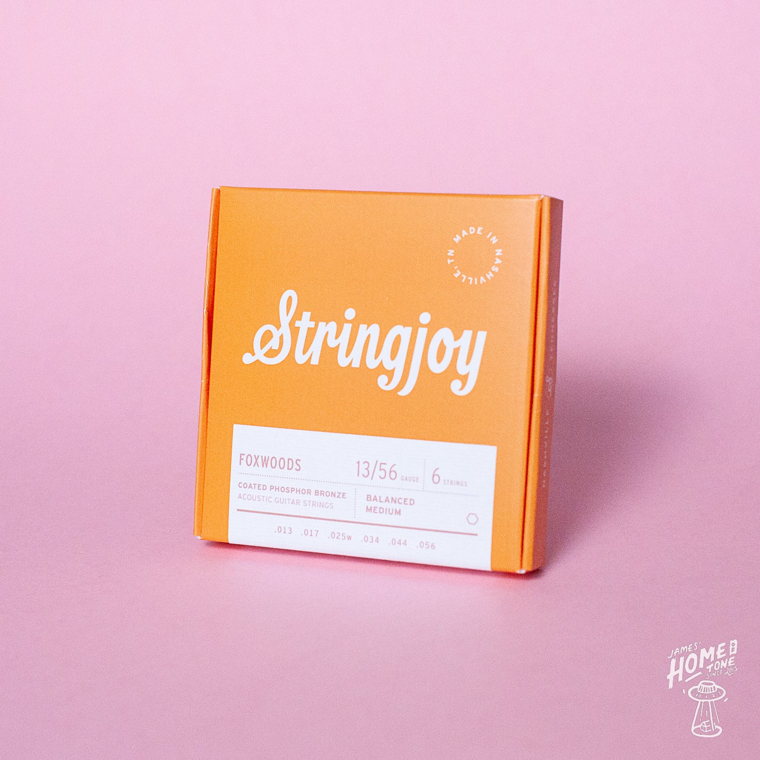Orange packaging of Stringjoy guitar strings on a pink background