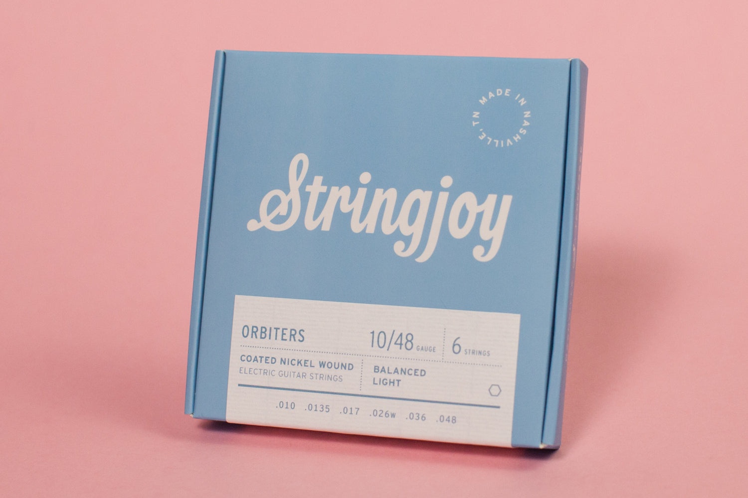 A pack of Stringjoy Orbiters coated nickel wound electric guitar strings with balanced light gauge, displayed against a pink background.