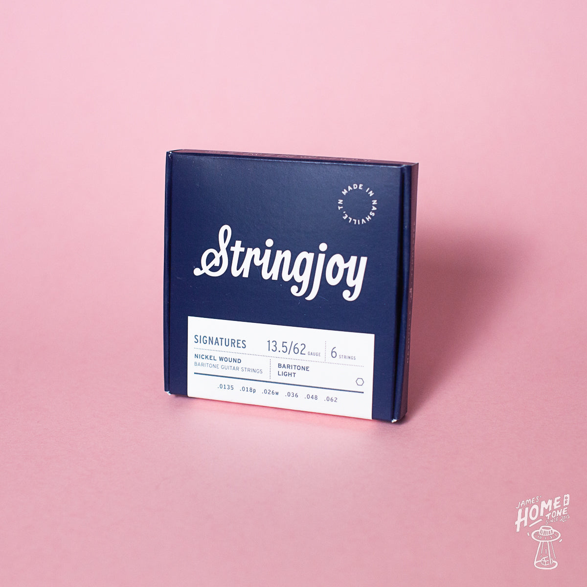 A box of Stringjoy baritone electric guitar strings in Nickel Wound version, with the gauges listed on the packaging, placed against a pink background.