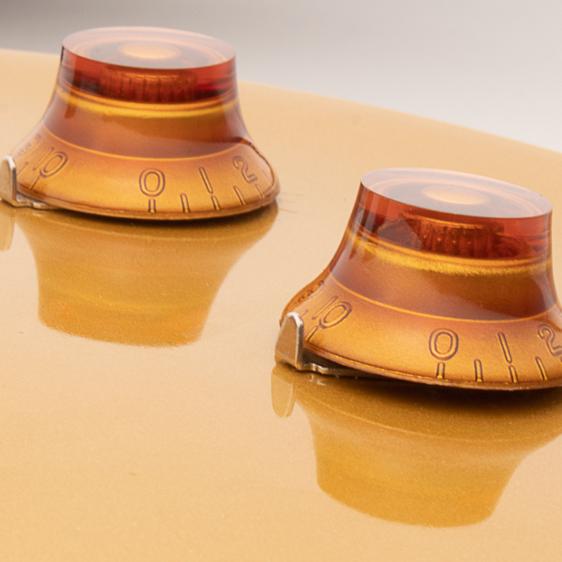 Two amber-colored knobs on a Gibson style guitar with pointer washers installed
