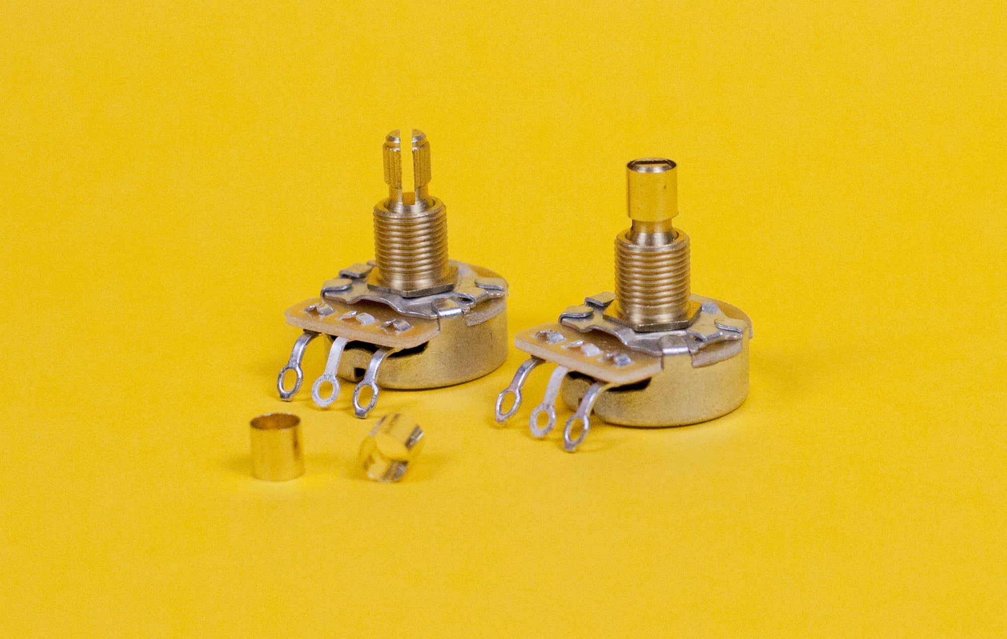 Two brass pot sleeves designed to convert split shaft pots to solid shaft pots, displayed on a yellow background.
