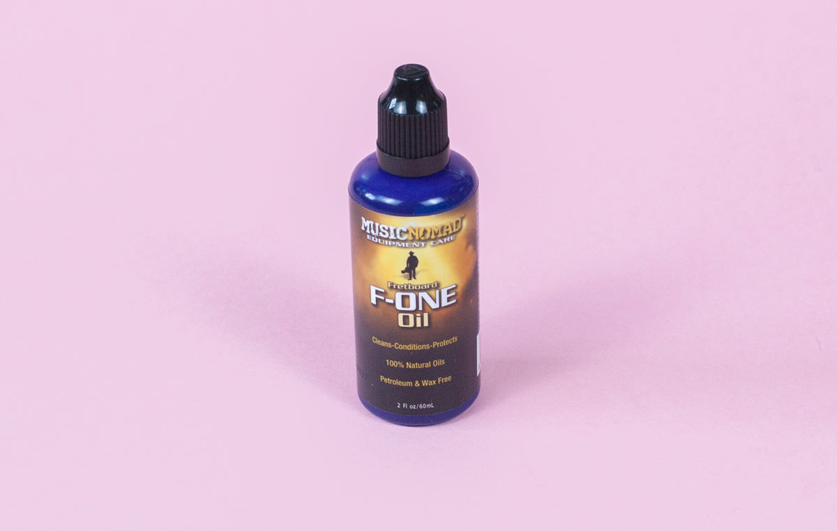 A bottle of MusicNomad Fretboard F-One Oil Cleaner & Conditioner on a pink background.