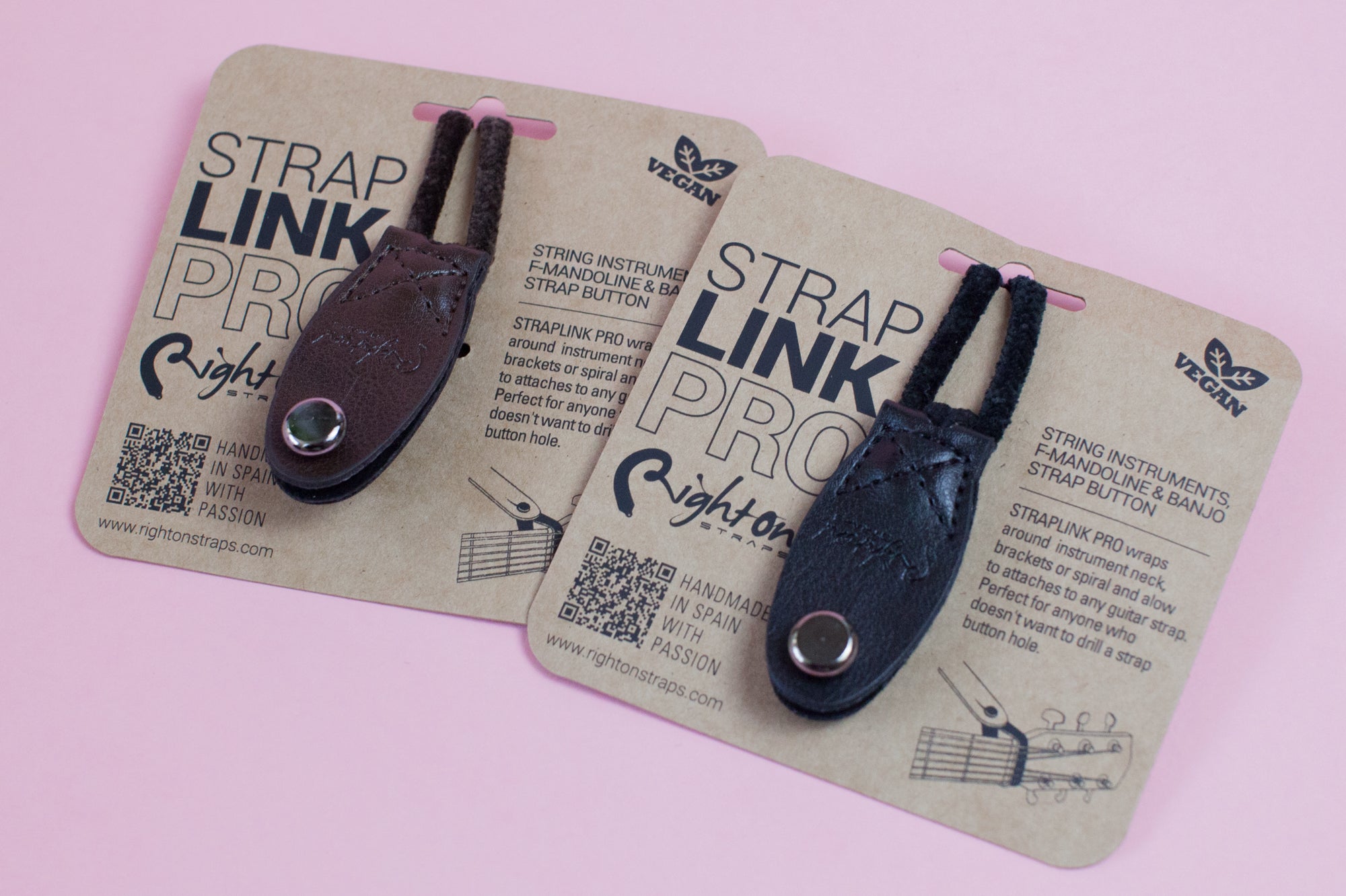 Two Neck Strap Link Pro accessories for guitars displayed on cardboard packaging, one brown and one black, on a pink background.