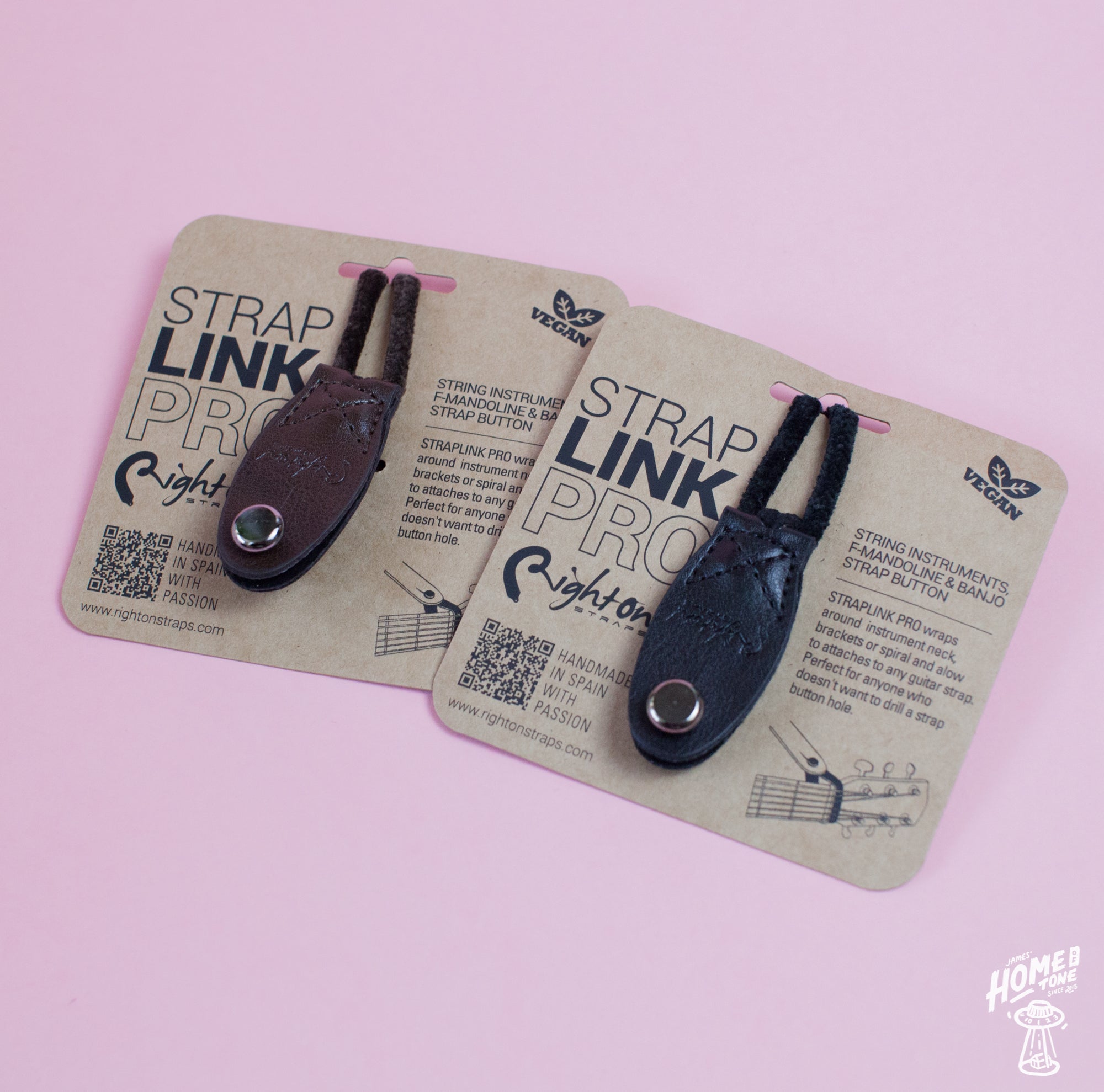 Two Neck Strap Link Pro accessories for guitars displayed on cardboard packaging, one brown and one black, on a pink background.