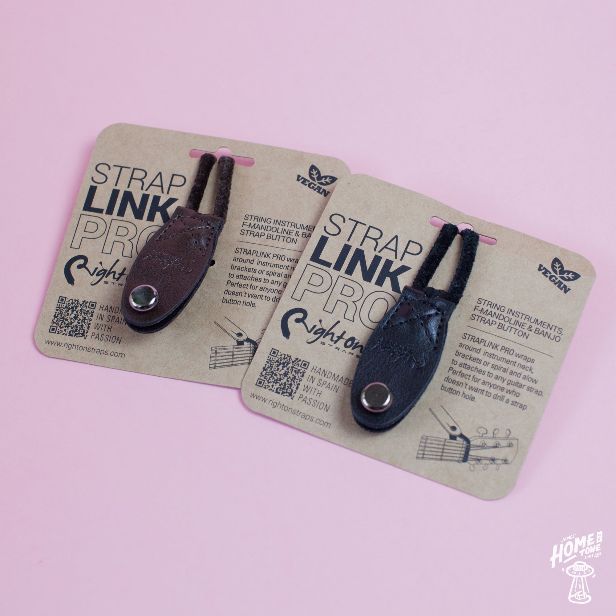 Two Neck Strap Link Pro accessories for guitars displayed on cardboard packaging, one brown and one black, on a pink background.