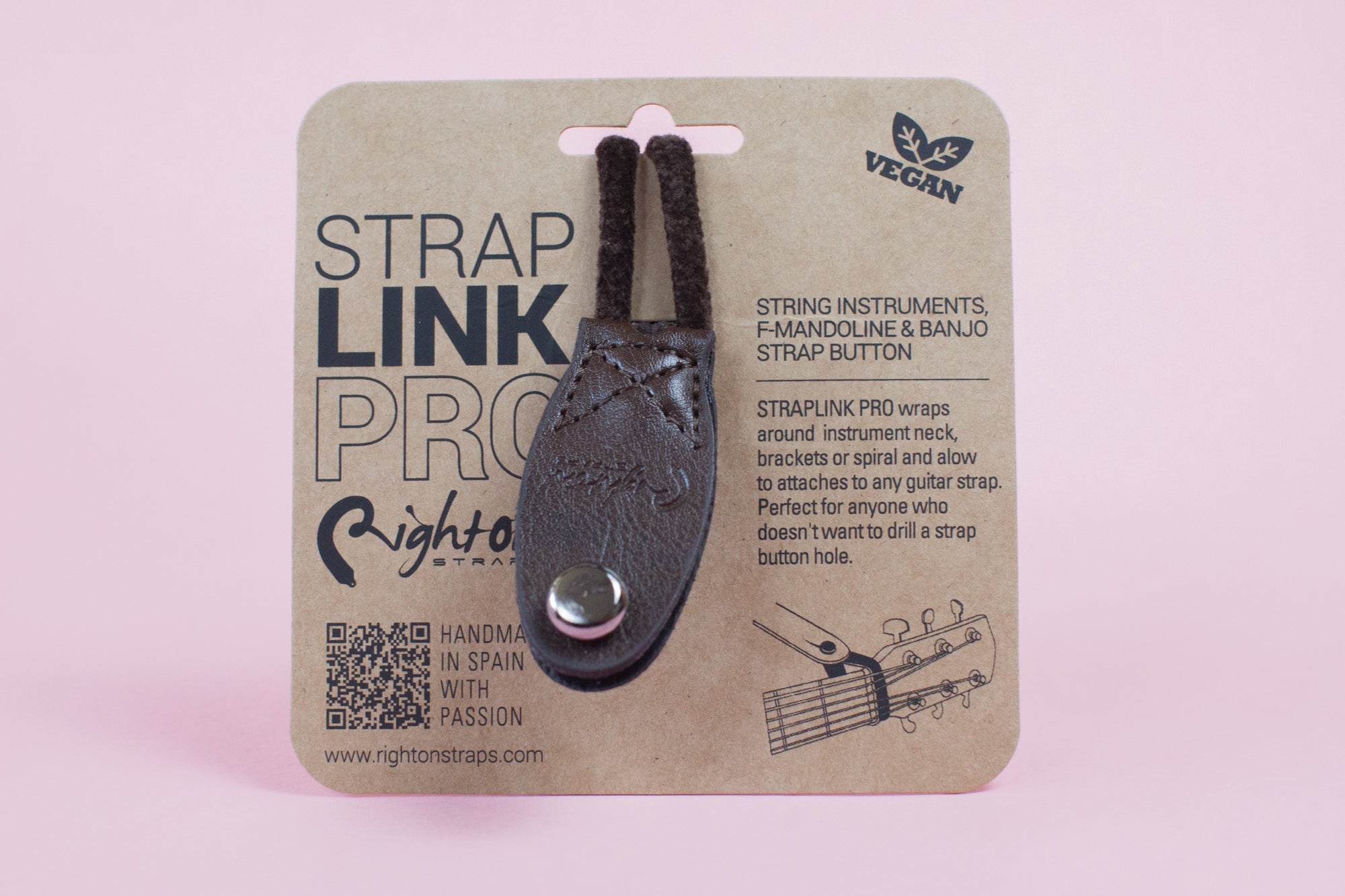 Neck Strap Link Pro accessories for guitars displayed on cardboard packaging, one brown and one black, on a pink background.