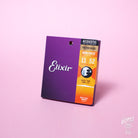 A pack of Elixir Nanoweb coated phosphor bronze acoustic guitar strings with gauges 11-52 displayed against a pink background.