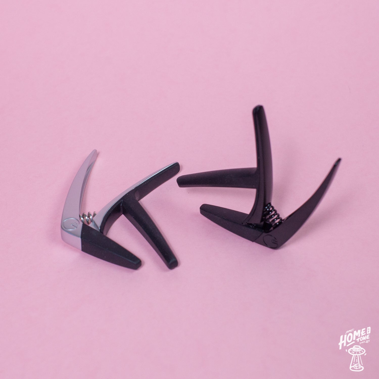 Two G7th - Nashville guitar capos with a silicone rubber and bar design, placed on a pink background.