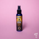 A spray bottle labeled 'Guitar ONE' by MusicNomad, designed for cleaning, polishing, and waxing gloss finishes on guitars. The bottle is on a pink background.