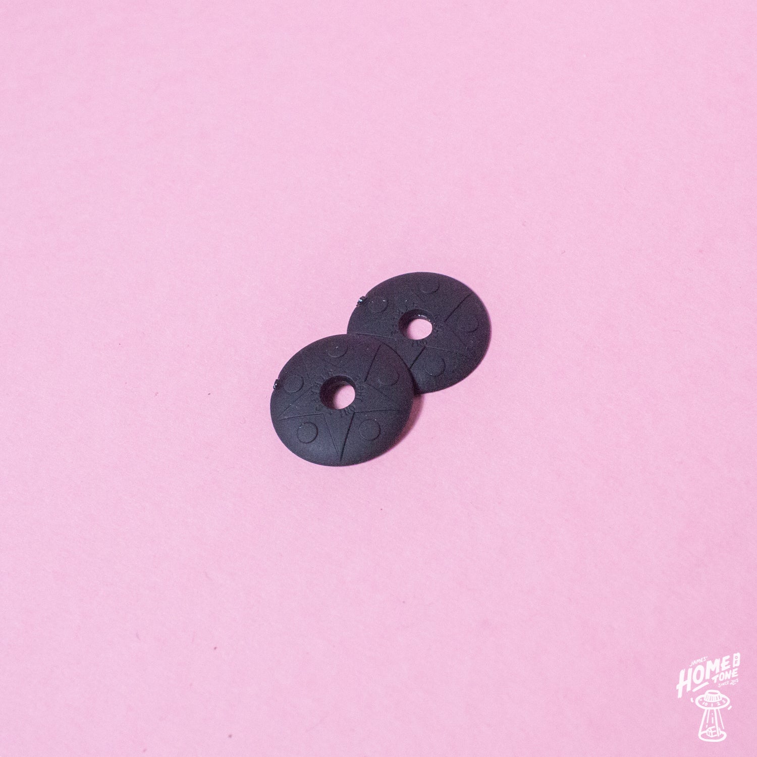 A pair of black rubber strap locks for guitars or basses, displayed on a pink background.