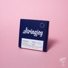 A box of Stringjoy Signature nickel wound electric guitar strings in Classic Light 10-46 gauge, placed against a pink background.