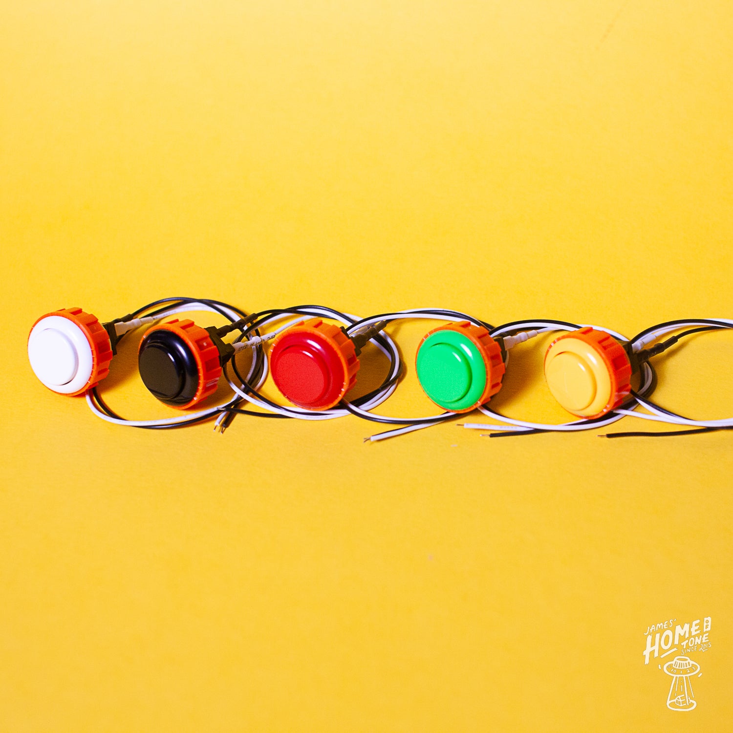 A series of colored Tesi Switch arcade buttons arranged in a line on a yellow background, each button connected to a wire.