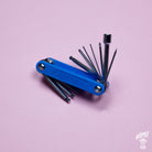 A blue CruzTOOLS GrooveTech multi-tool for guitars and basses, displayed with its various tools extended, against a pink background.