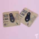 Two leather end-pin jack strap links on cardboard packaging, one brown and one black, with branding and product information.