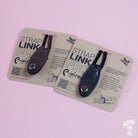 Two Neck Strap Link Pro accessories for guitars displayed on cardboard packaging, one brown and one black, on a pink background.