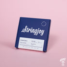 A box of Stringjoy Signature nickel wound electric guitar strings in balanced light gauge, displayed against a pink background.