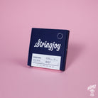 A box of Stringjoy Signature nickel wound electric guitar strings in medium gauge, displayed against a pink background.